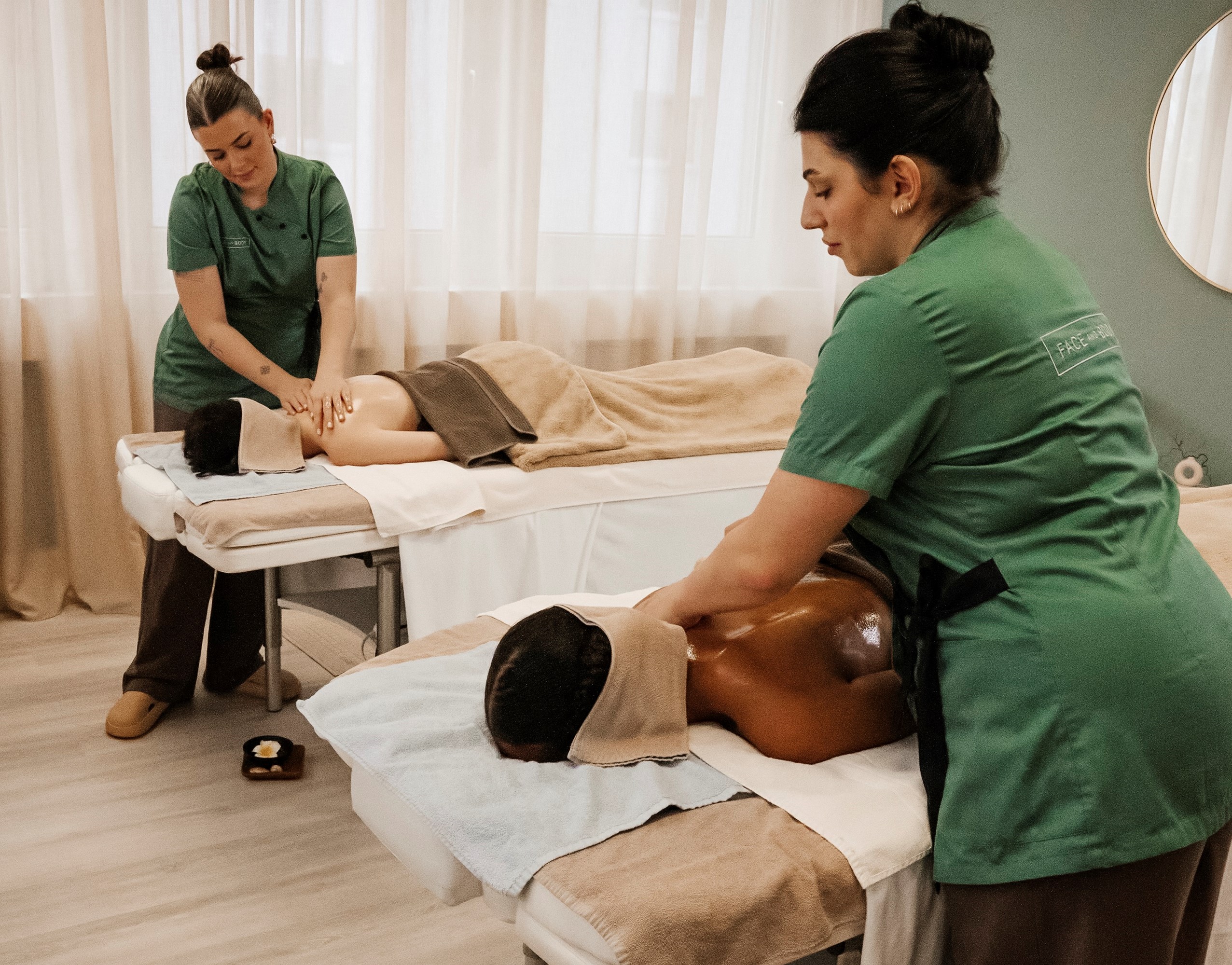 Zwei Personen bei gleichzeitiger Paarmassage auf nebeneinanderliegenden Liegen